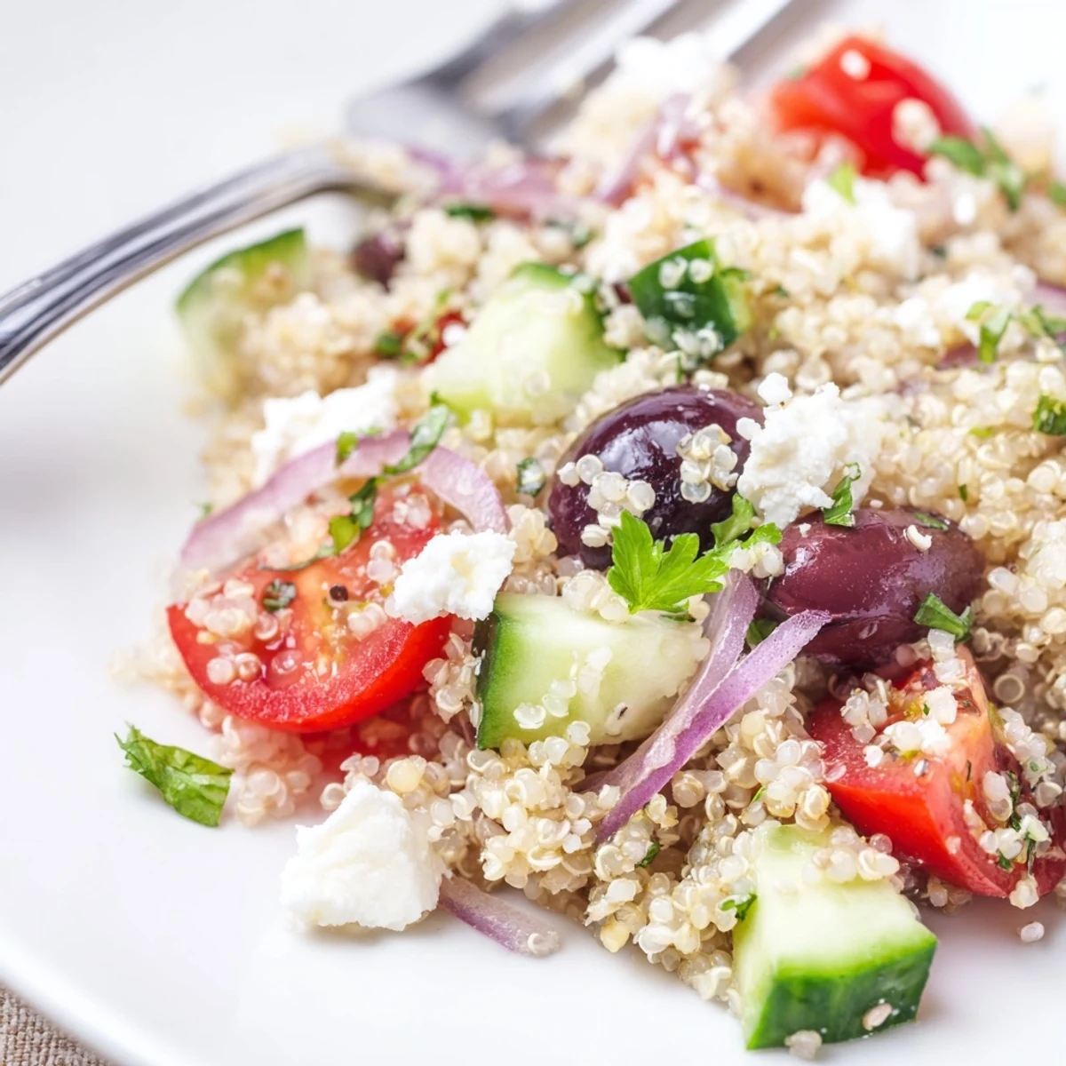 A vibrant Mediterranean Quinoa Salad with Cucumber and Feta in a white bowl, featuring chopped cucumbers, halved cherry tomatoes, and crumbled feta cheese.