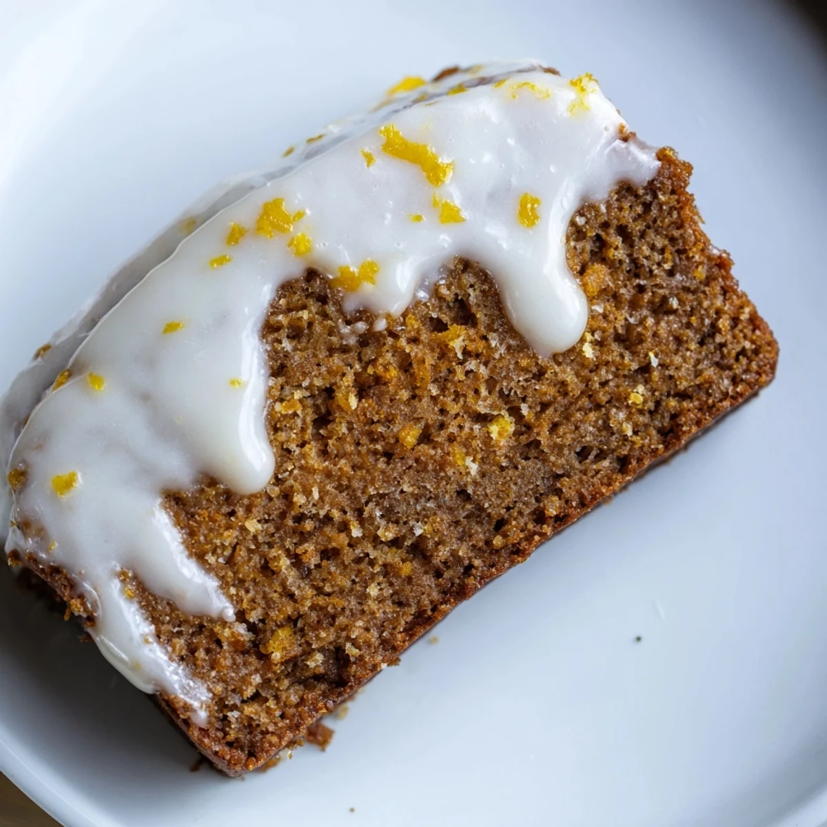 Overhead view of Gingerbread Loaf with Lemon Cream Cheese Glaze, topped with fresh zest and festive cranberries.