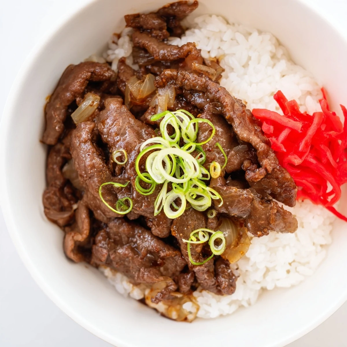 Savory beef and onion mixture simmering in a rich sauce over a bowl of fluffy white rice.