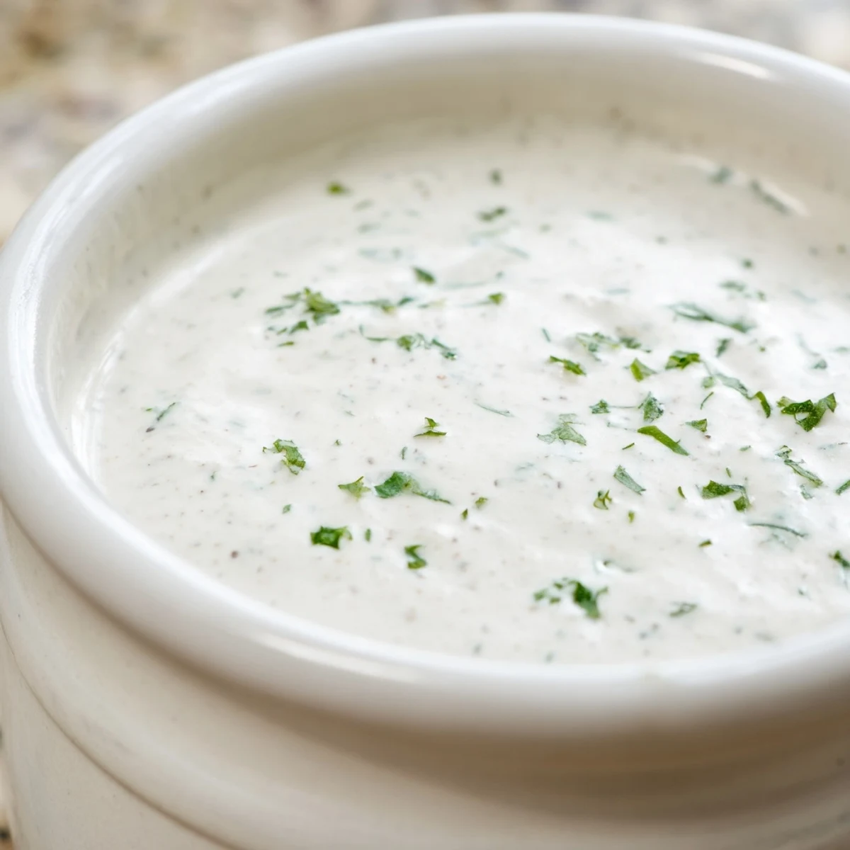 A jar of homemade Creamy Salad Dressing with a whisk beside a small bowl for dipping crunchy fresh vegetable sticks.