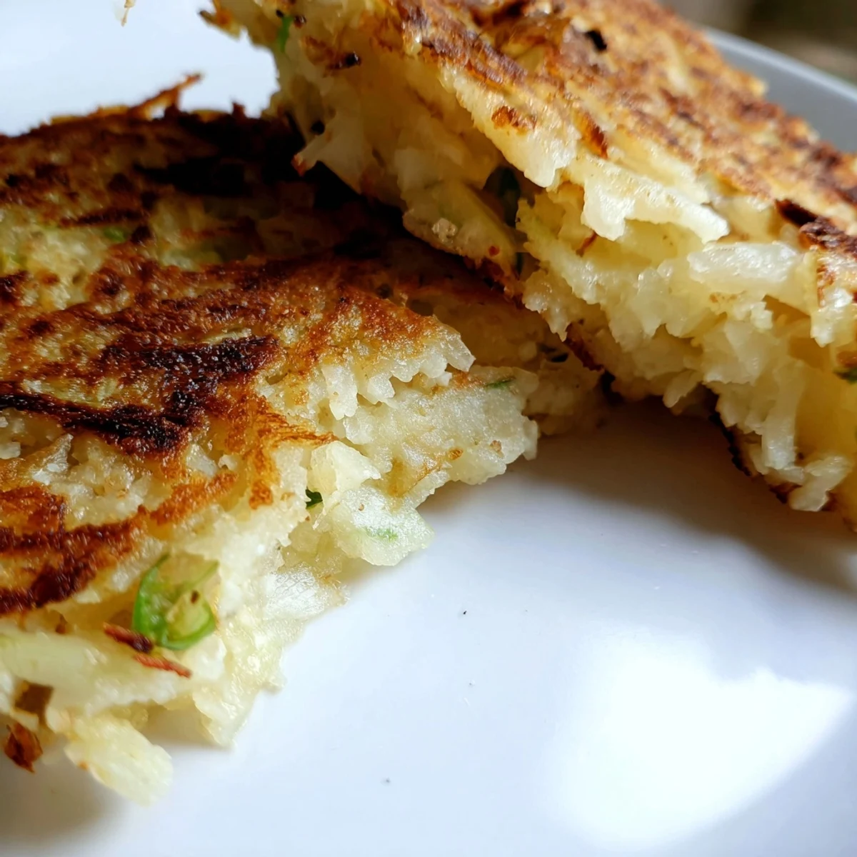 Golden-brown Irish Potato Cakes with Scallions sizzling in a pan, showing a crisp, fluffy texture with visible green onion specks.  
