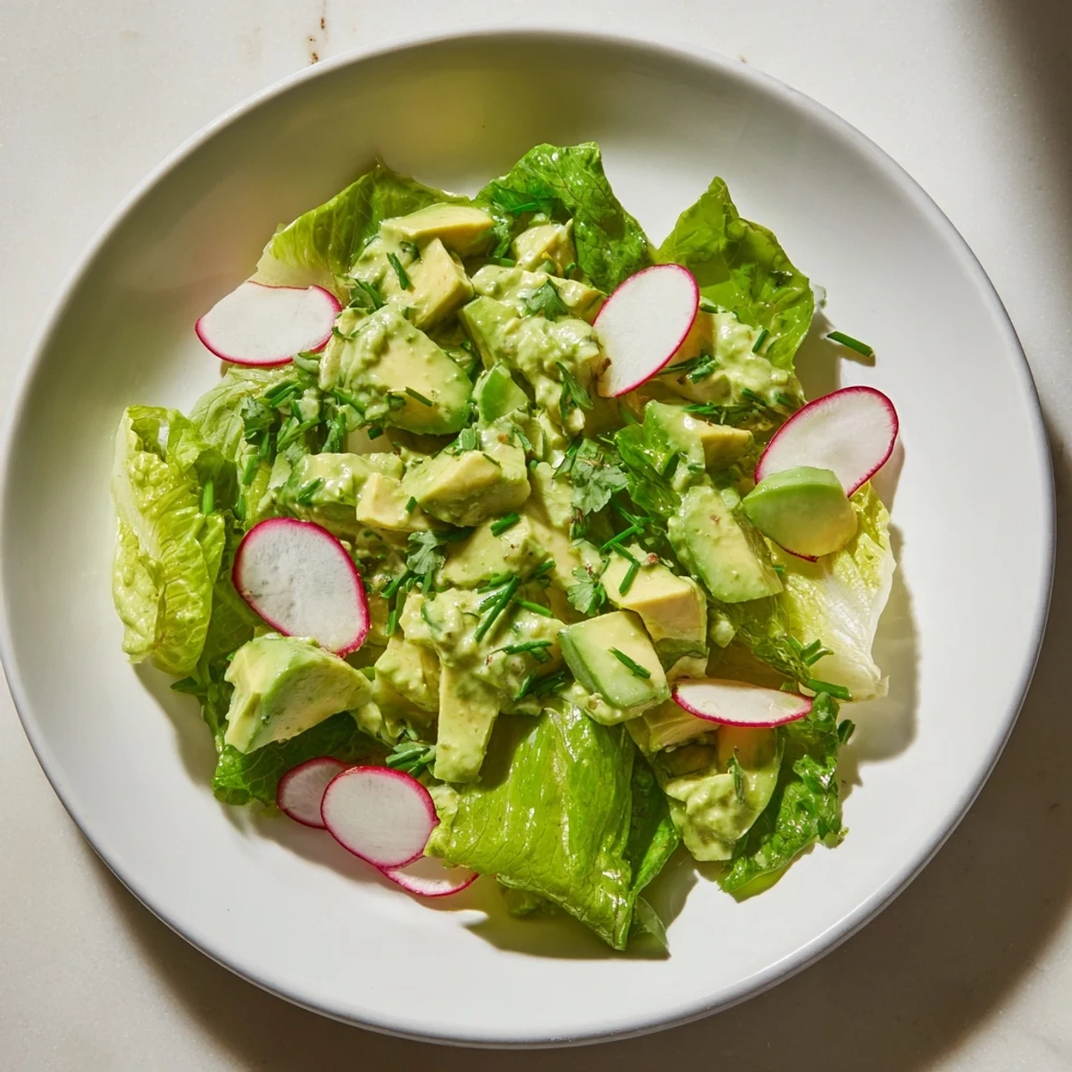 Freshly prepared Green Goddess Salad featuring avocado and cucumber, garnished with herbs and sunflower seeds for crunch.