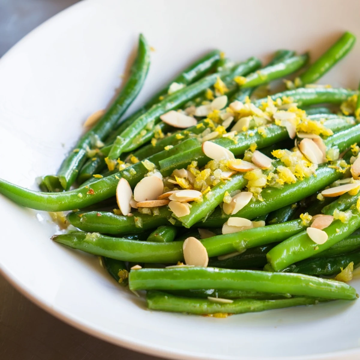 Vibrant crisp-tender Green Beans with Lemon and Toasted Almonds plated beside roasted chicken, sprinkled with sea salt and fragrant lemon zest.