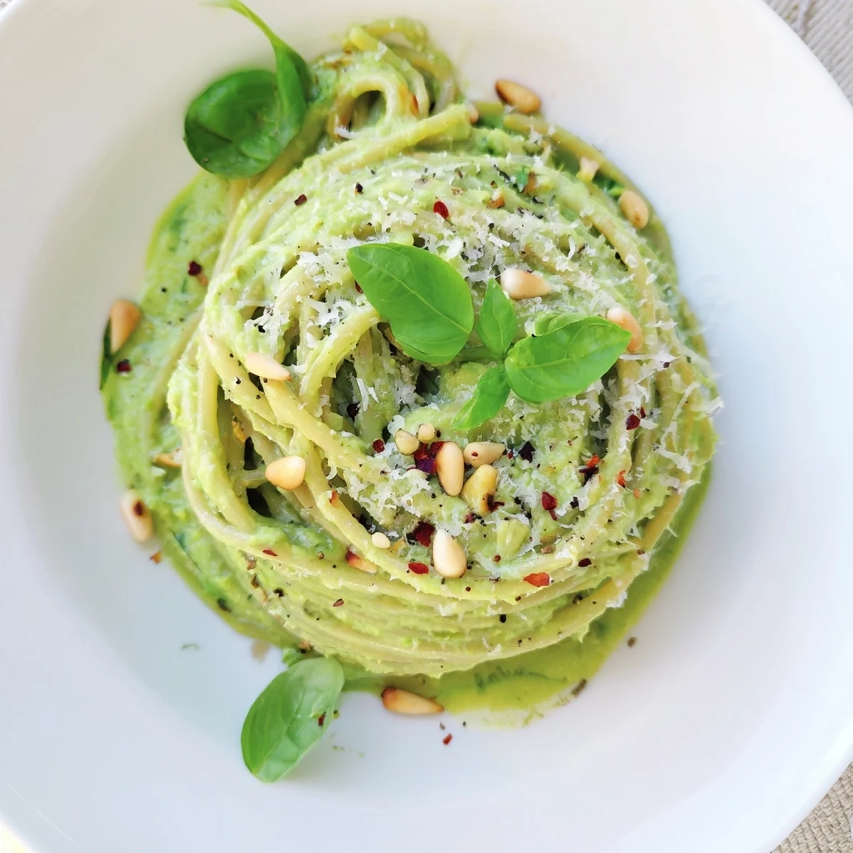 Creamy avocado and spinach pasta twirled on a fork, with a velvety green sauce clinging to each strand and fresh basil garnish.