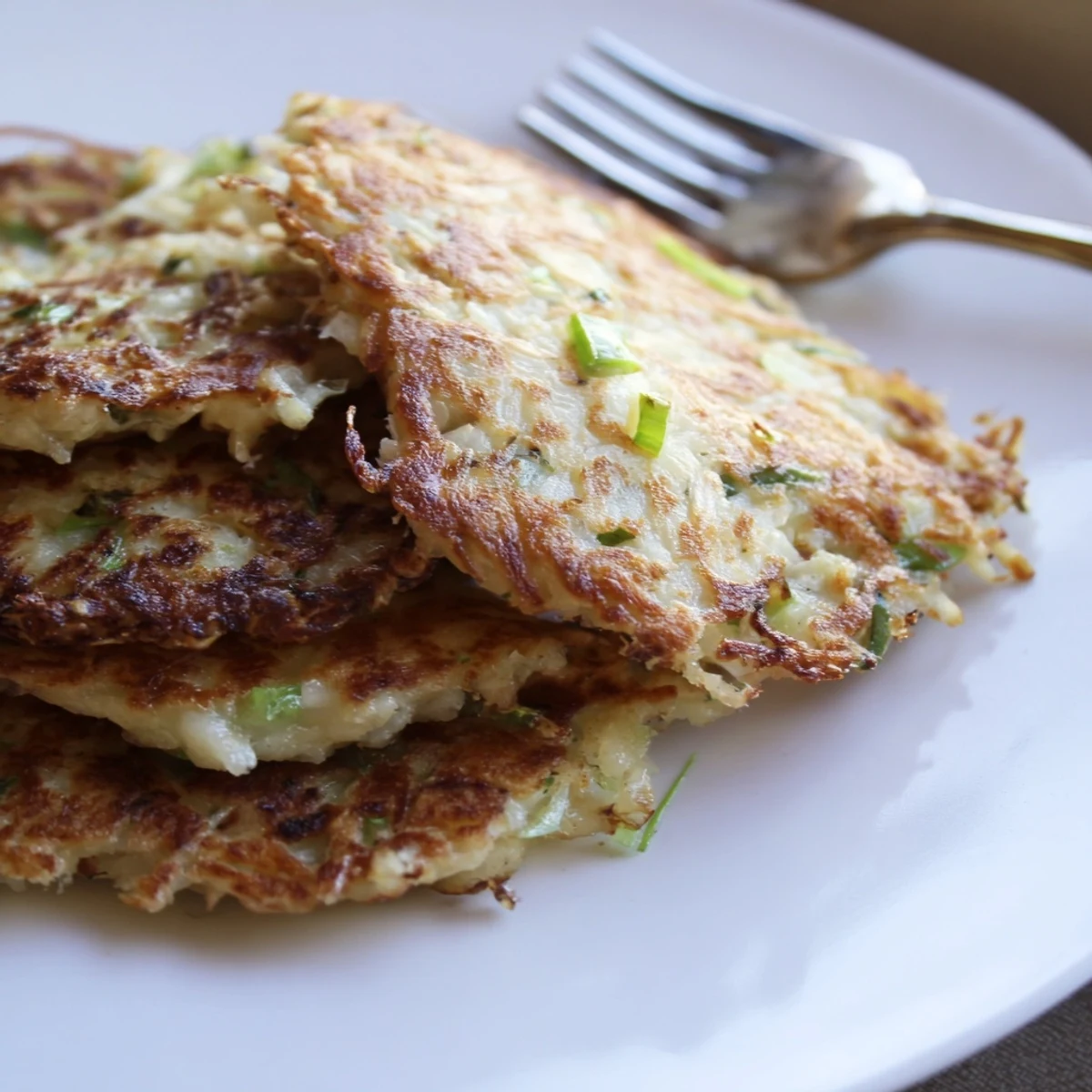 Stack of homemade Irish Boxty Potato Pancakes with Scallions, their fluffy interior and crunchy exterior highlighted on a rustic plate.