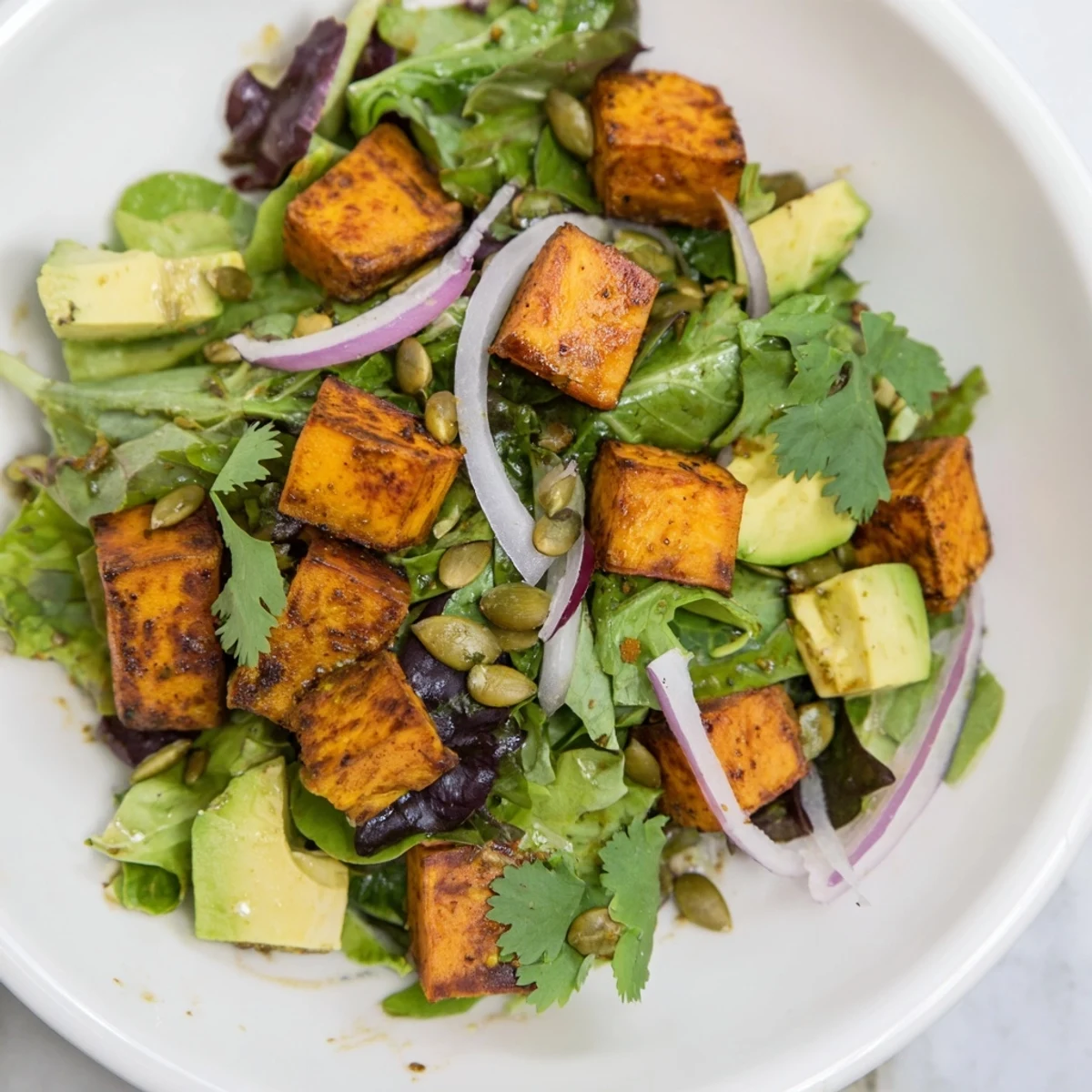 Golden roasted sweet potatoes sit atop fresh greens with diced avocado and red onion in Roasted Sweet Potato Salad with Lime Dressing.