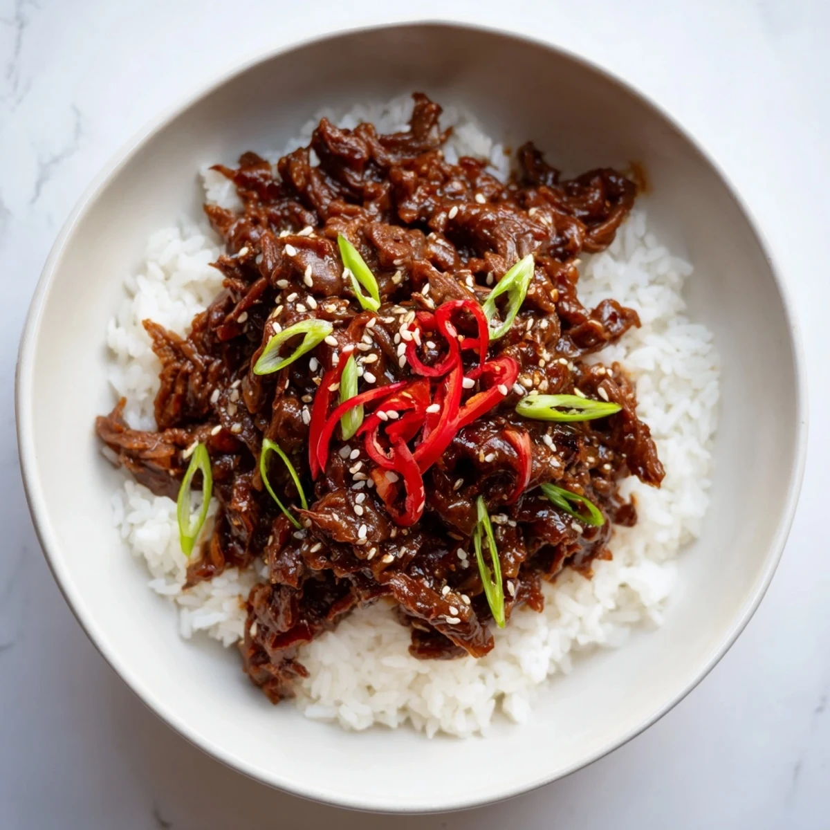 Shredded Slow Cooker Korean Beef glistens with savory-sweet sauce, served over steamed white rice with green onions.