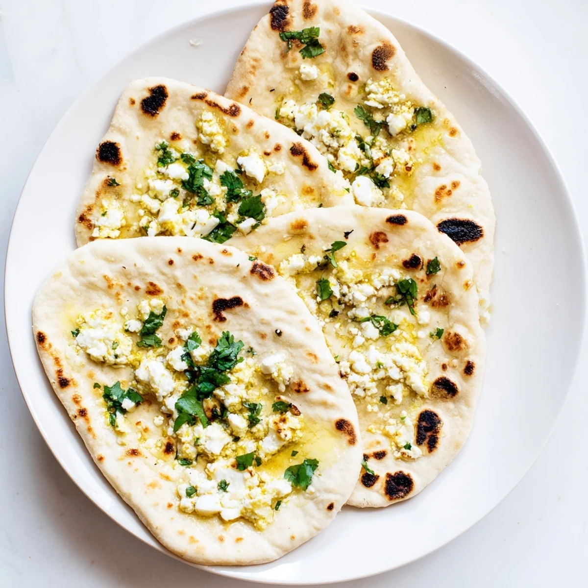 Freshly baked Cottage Cheese Garlic Naan with visible green cilantro and garlic flecks on a plate.