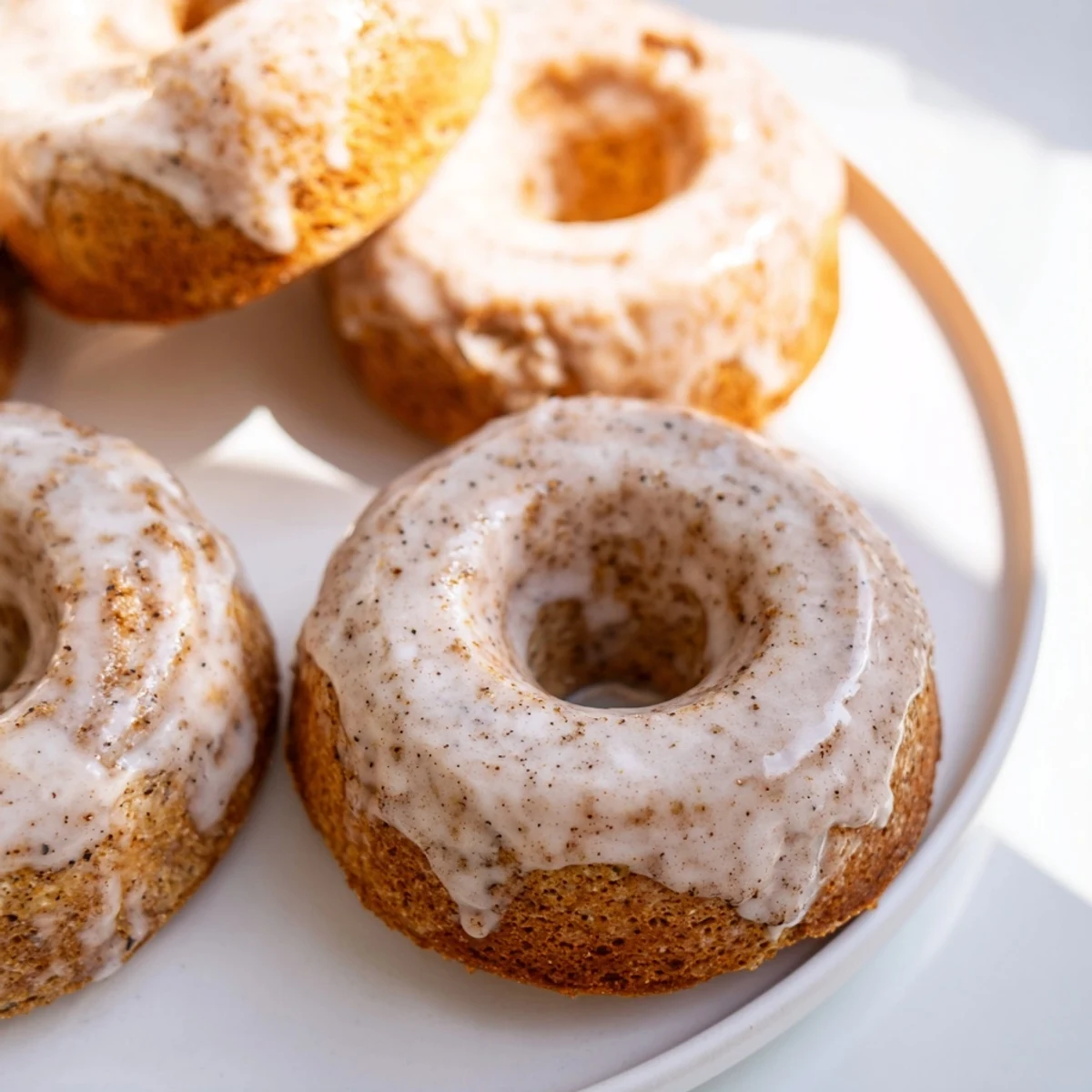 Warm Baked Banana Bread Donuts on a wire rack, glazed with white icing and sprinkled with cinnamon sugar for a cozy breakfast treat.