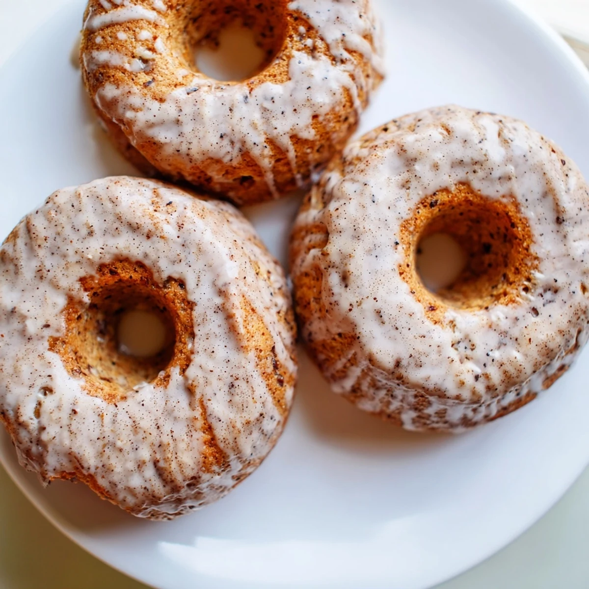 A close-up of moist Baked Banana Bread Donuts topped with a vanilla glaze, served alongside a steaming mug of coffee on a rustic table.