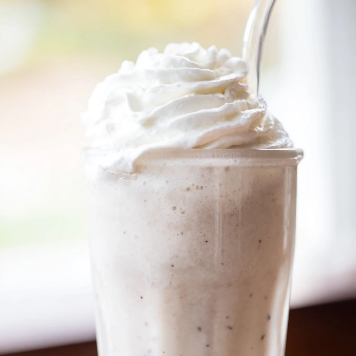 Blended Starbucks Vanilla Bean Frappuccino with ice cubes and vanilla ice cream, ready to serve with a straw.