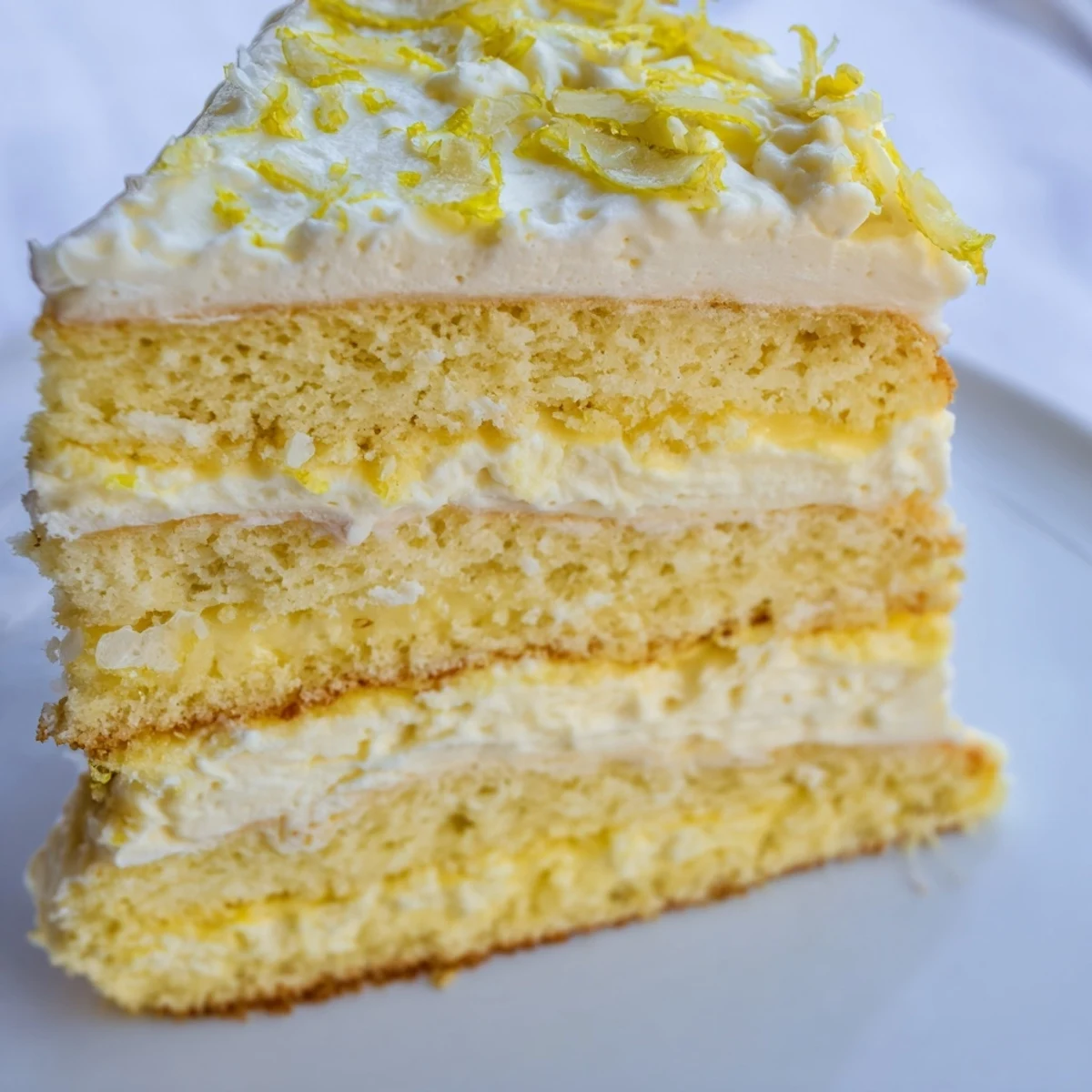 Golden layers of Limoncello Mascarpone Cake reveal soaked sponge, creamy filling, and fresh lemon zest garnish on a white plate.