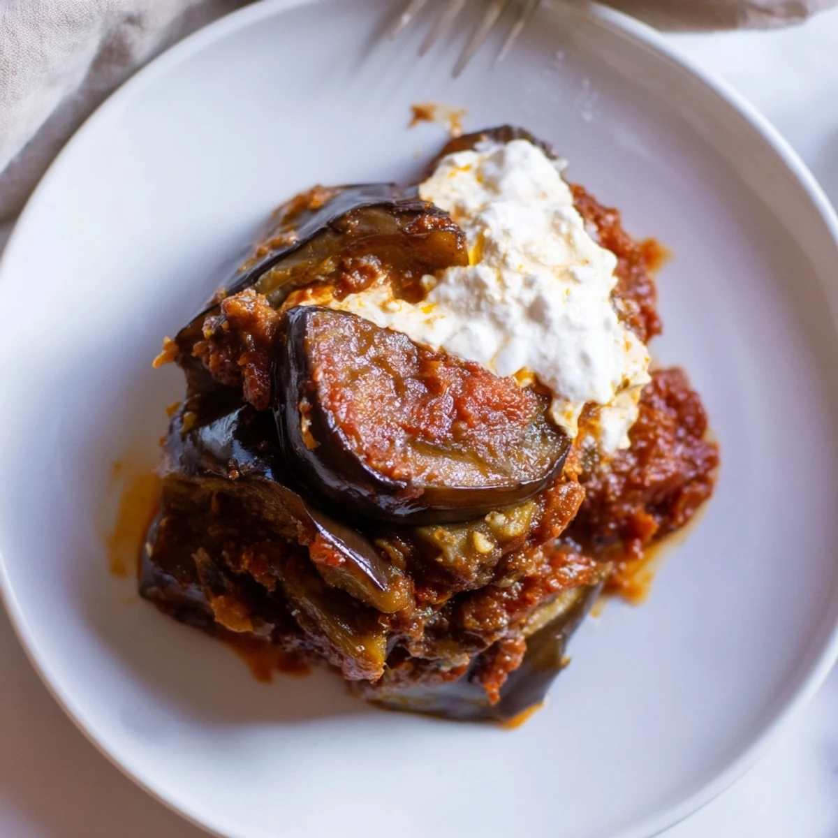 Close-up of Borani Banjan in a baking dish, featuring golden eggplant and a rich, spiced tomato layer.