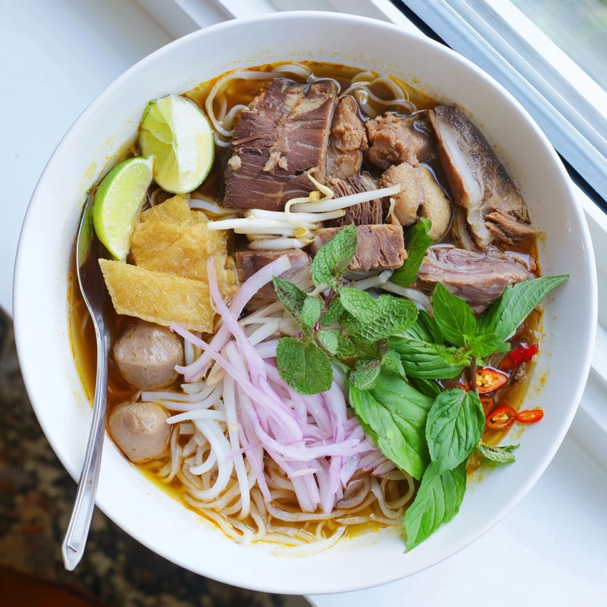 Close-up of Bun Bo Hue with fresh herbs, bean sprouts, and vibrant chili oil drizzled on top.