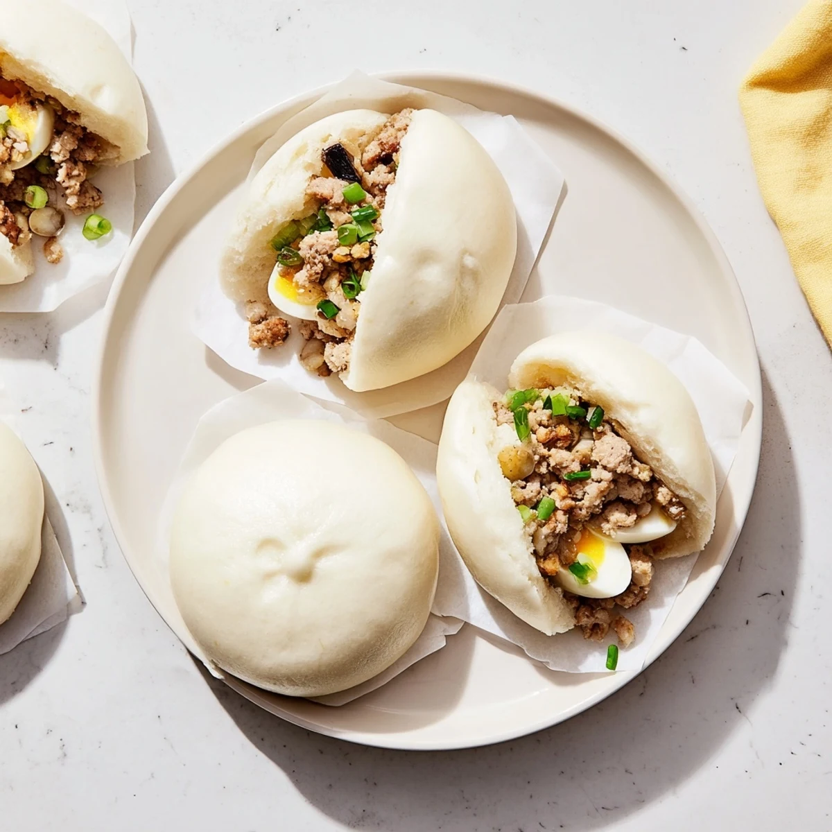Steamed Banh Bao buns resting on parchment paper, revealing tender dough and a hearty pork filling.  