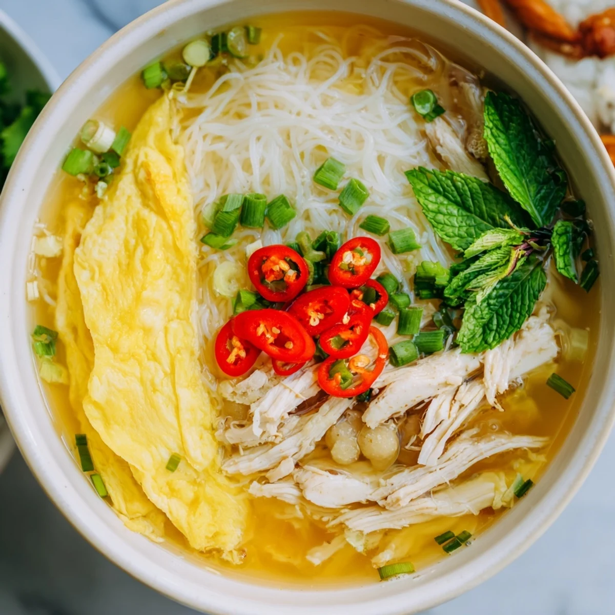 Bright herbs and lime wedges garnish a serving of Bun Thang, a comforting Vietnamese noodle soup for a weeknight meal.