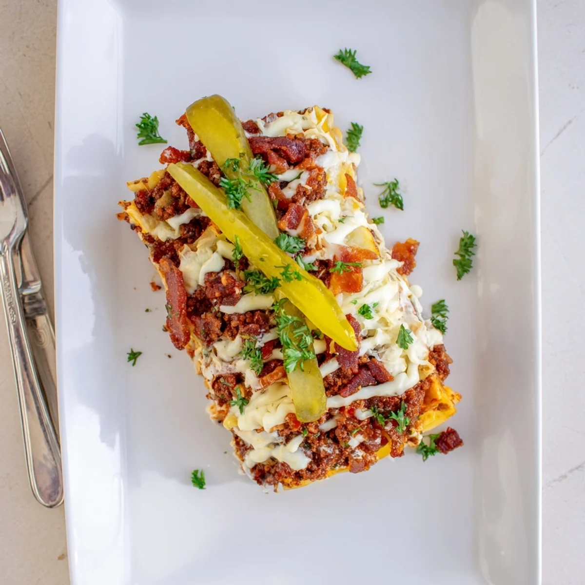 Hearty square of Lasagna Meets Cheeseburger Parmesan Garlic Bacon Style garnished with parsley, served beside fresh green salad.