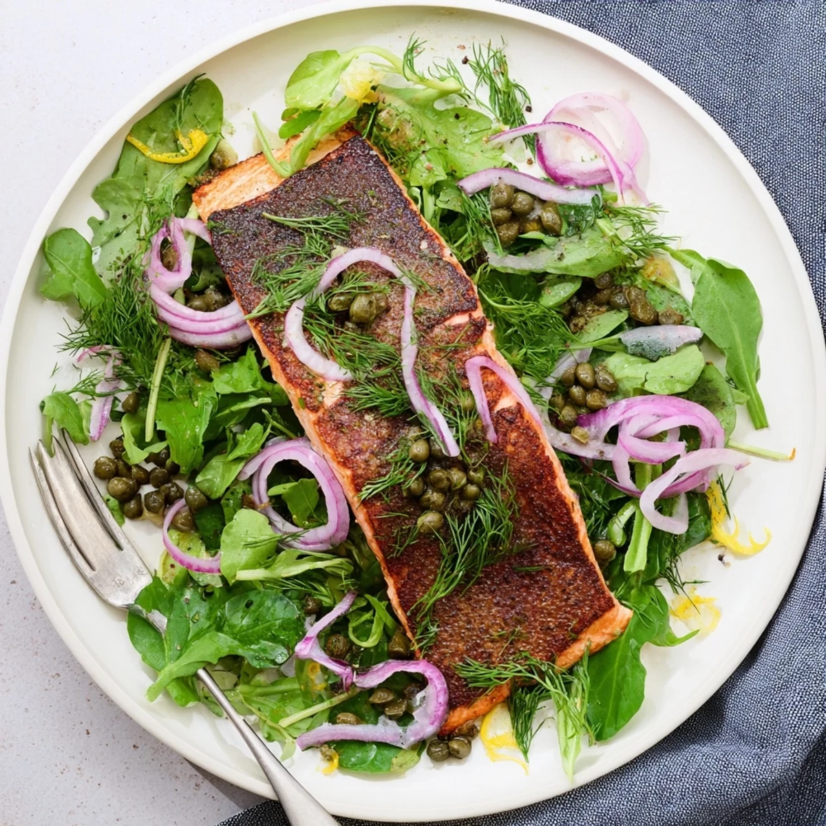 Golden-brown Crispy Skin Tasmanian Atlantic Salmon fillets with fresh dill and parsley garnish on a bed of mixed greens.