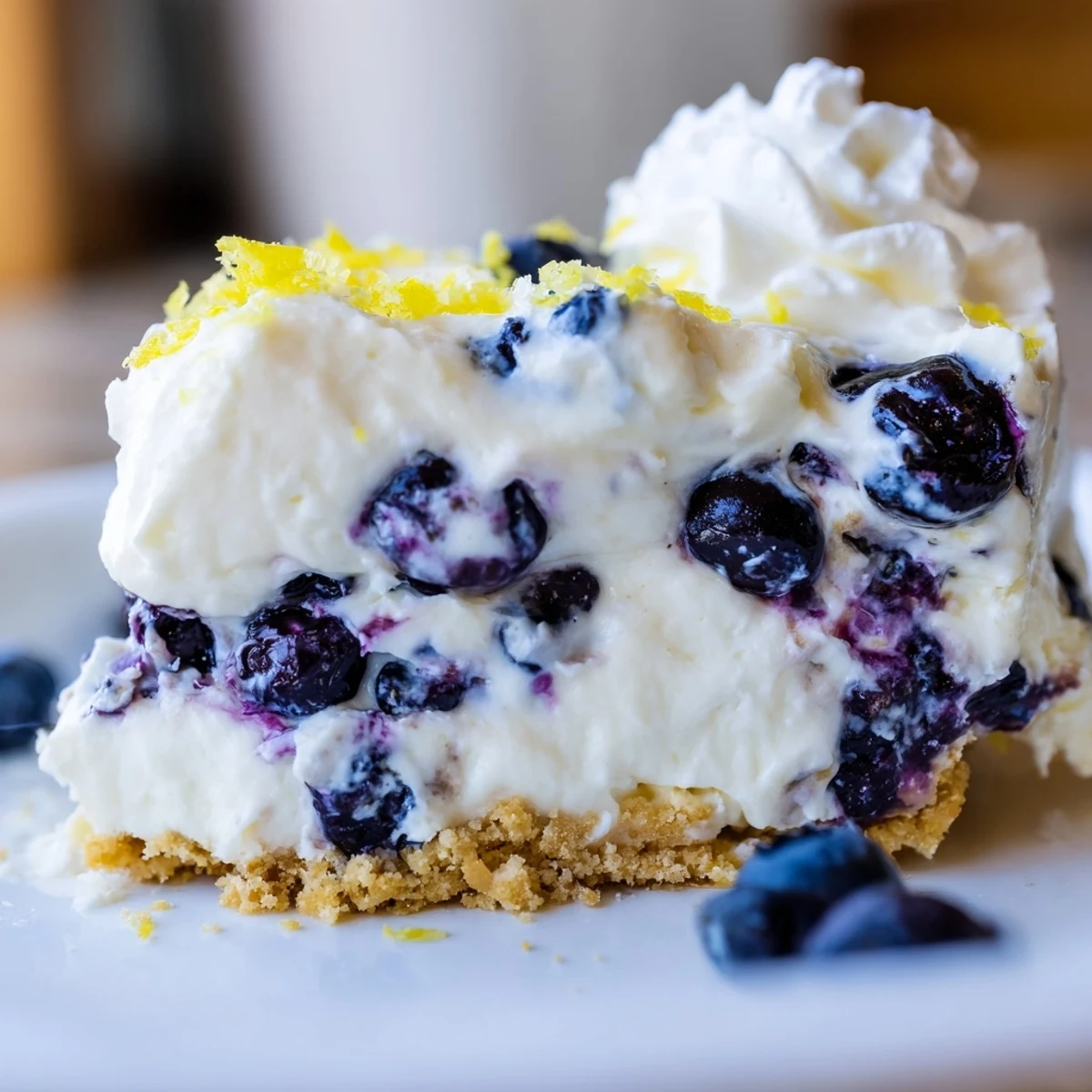 Slice of refreshing lemon blueberry cream cake with whipped cream and blueberry garnish on white plate