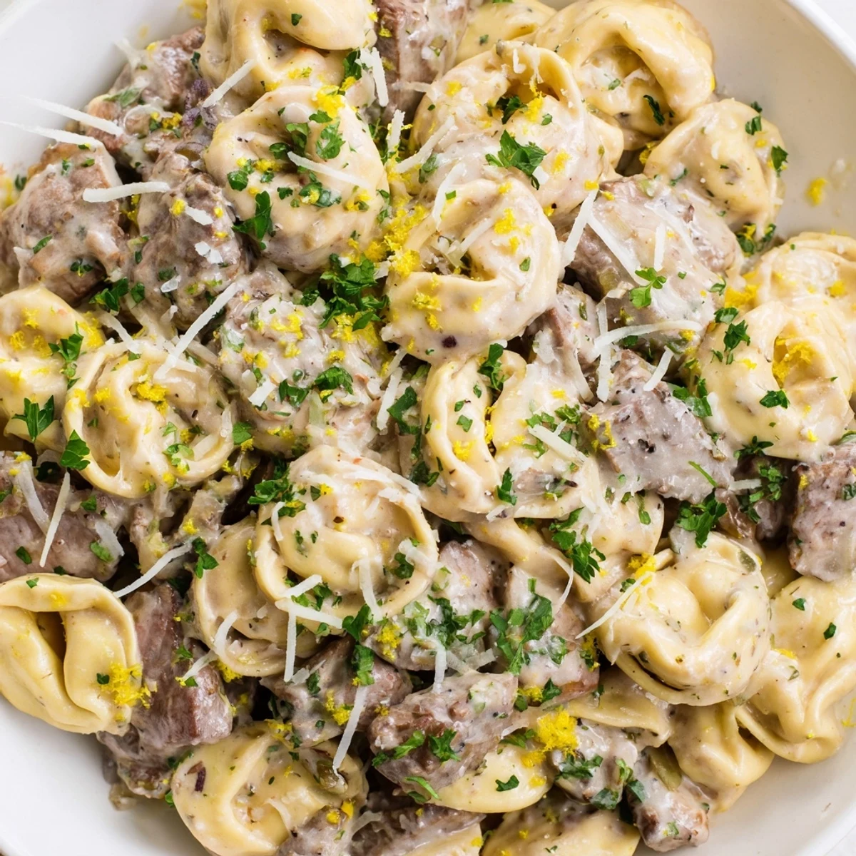 Golden garlic steak tortellini in creamy parmesan sauce topped with fresh parsley and lemon zest