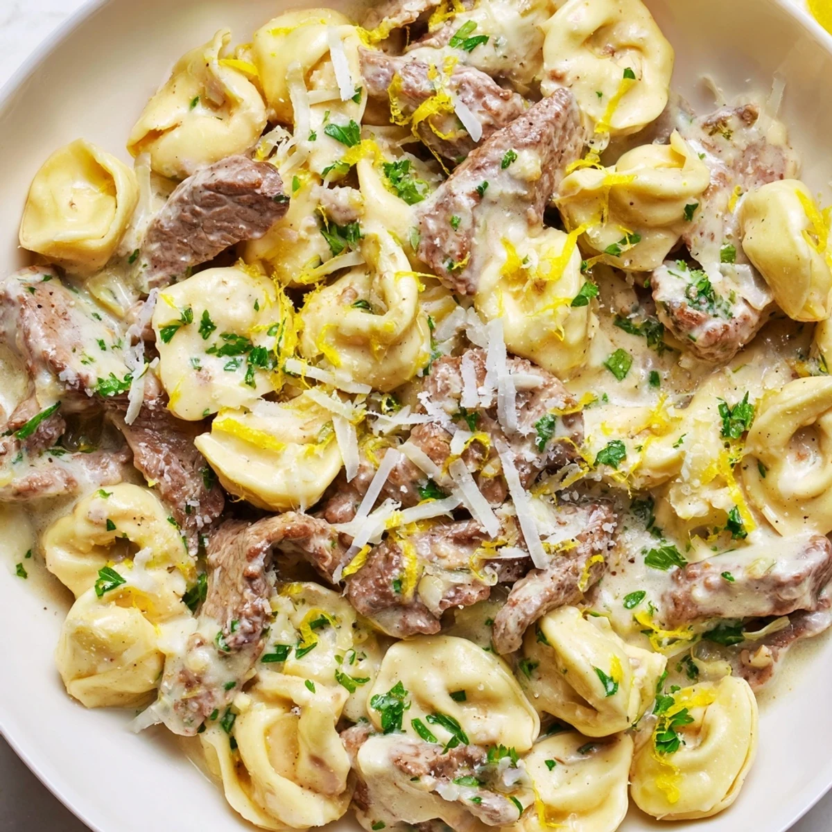 Sliced steak tortellini pasta tossed in rich garlic cream sauce with cracked black pepper garnish