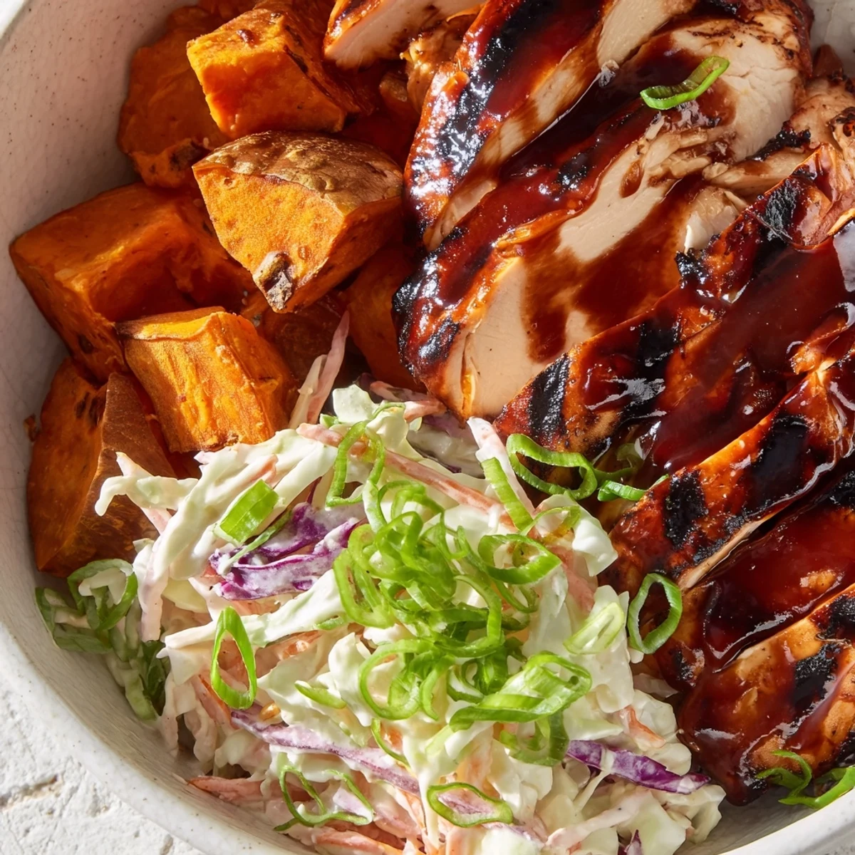 Colorful BBQ chicken bowls featuring tender roasted sweet potatoes and crunchy purple cabbage slaw