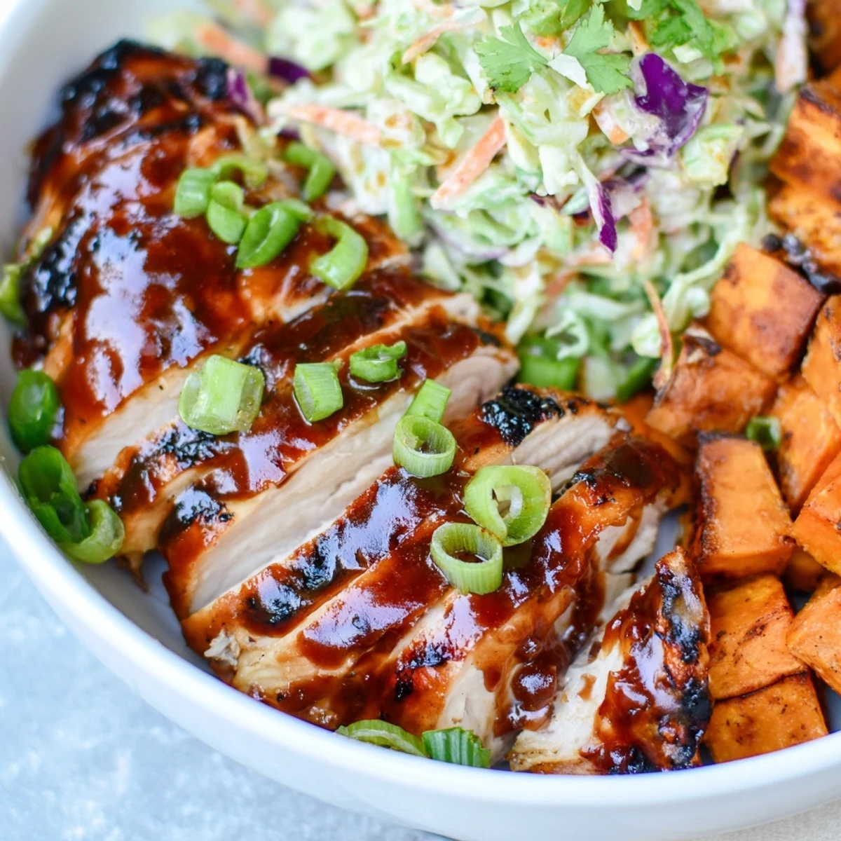 Hearty BBQ chicken bowl with golden roasted sweet potatoes topped with fresh cilantro and lime wedges