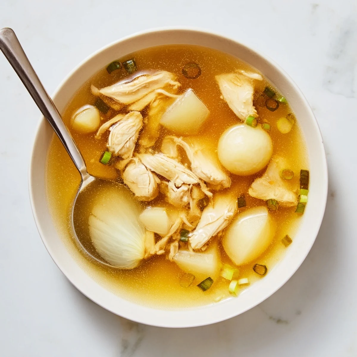 Golden bowl of Dakgomtang Korean chicken soup garnished with fresh green onions and served alongside tangy dipping sauce