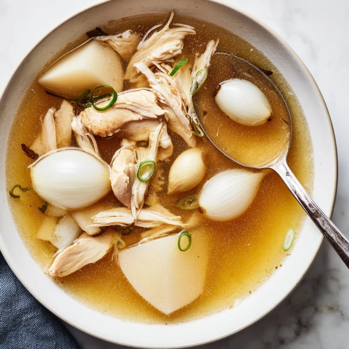 Steaming Dakgomtang featuring tender shredded chicken in clear broth topped with scallions and sesame seeds