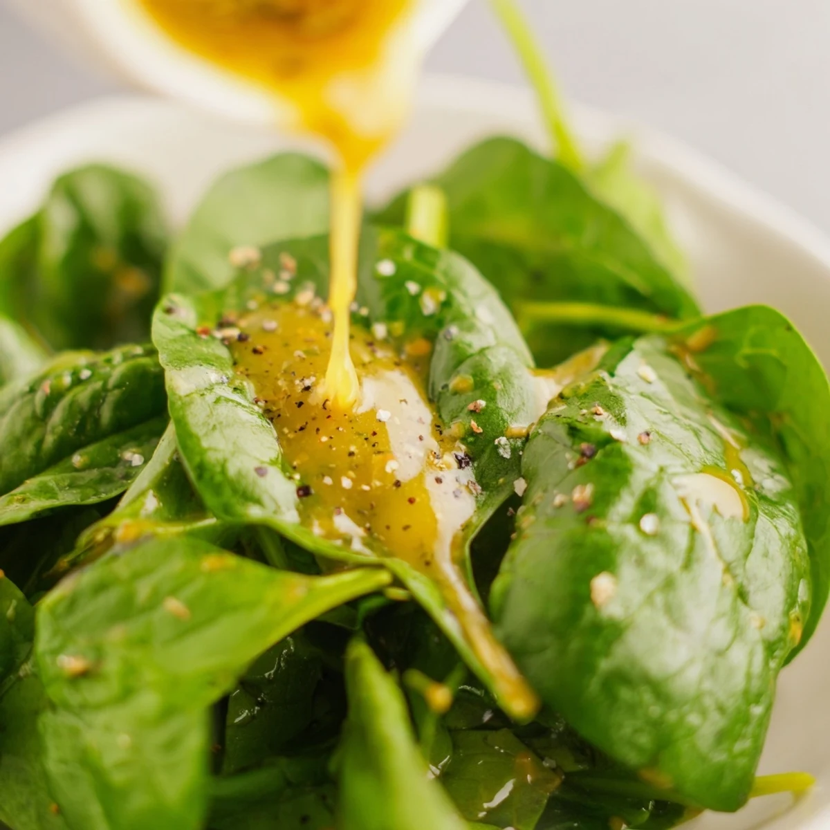 Golden honey lemon vinaigrette drizzled over fresh mixed greens in a white bowl