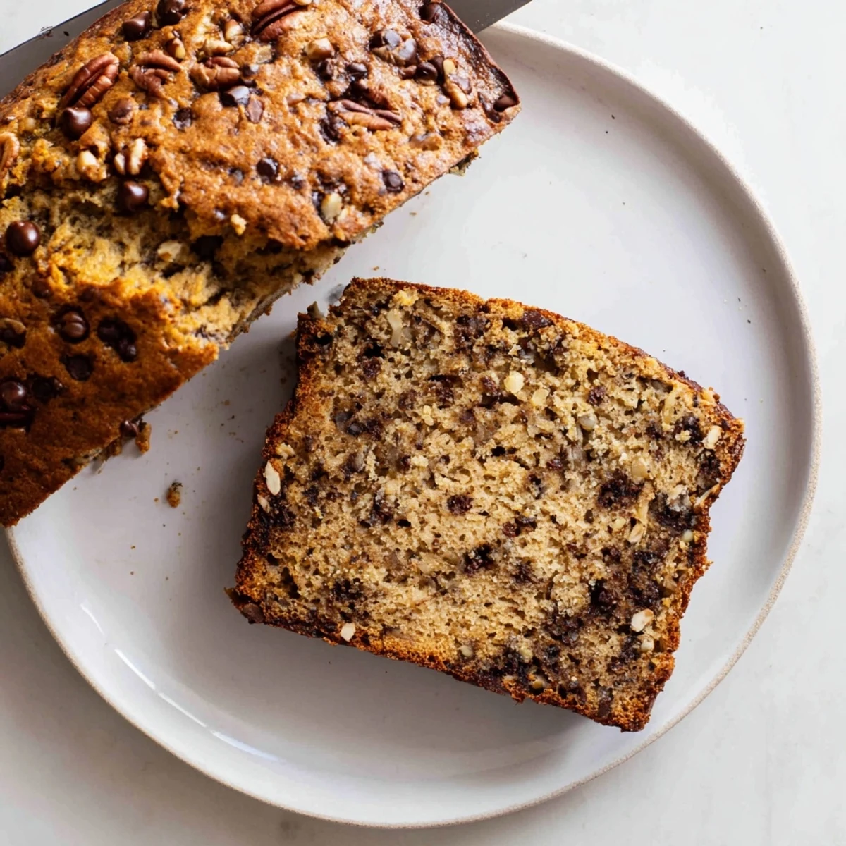Thick slice of moist chocolate chip banana bread displaying speckled banana flesh and scattered chocolate morsels