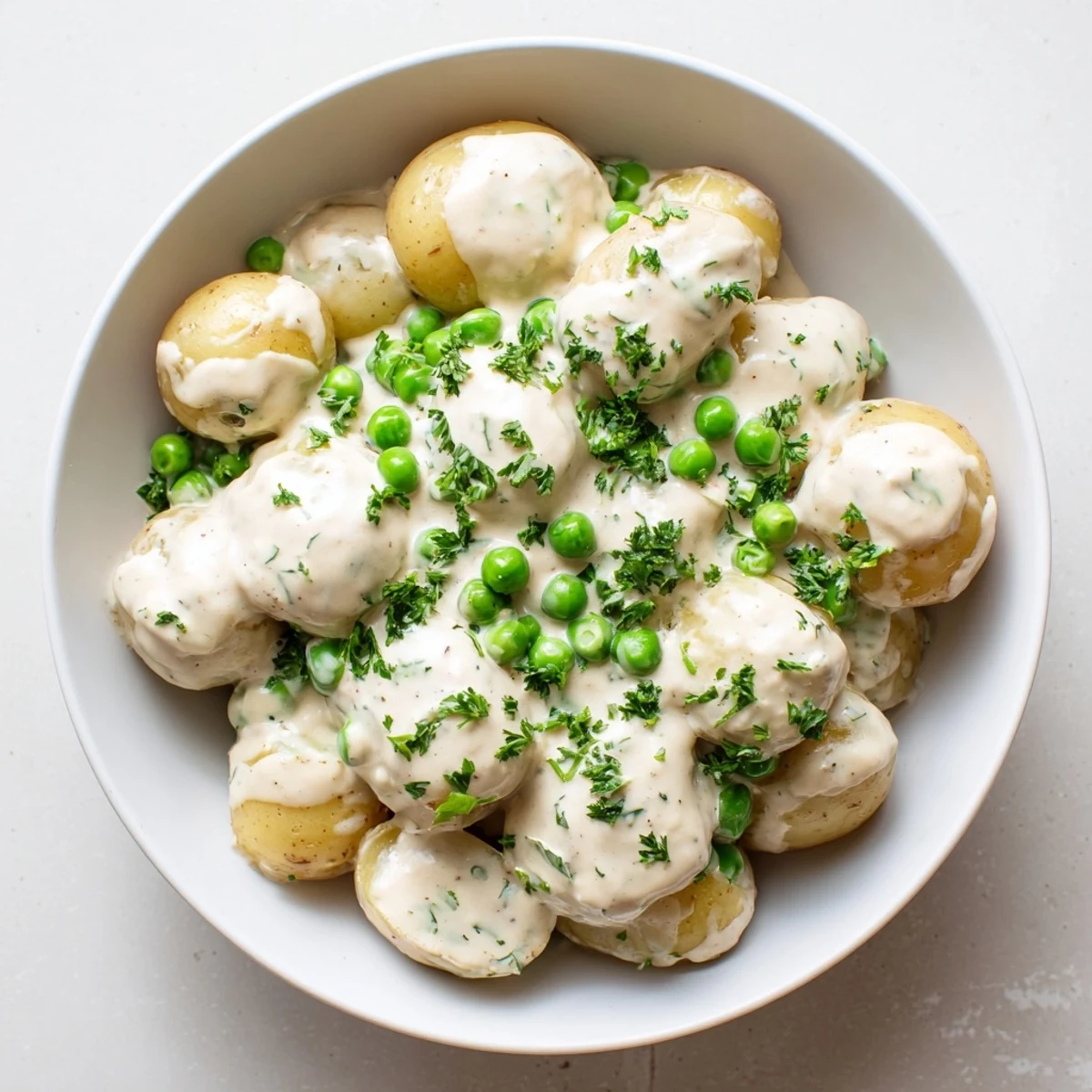 Creamed peas and potatoes in a white bowl garnished with fresh green parsley