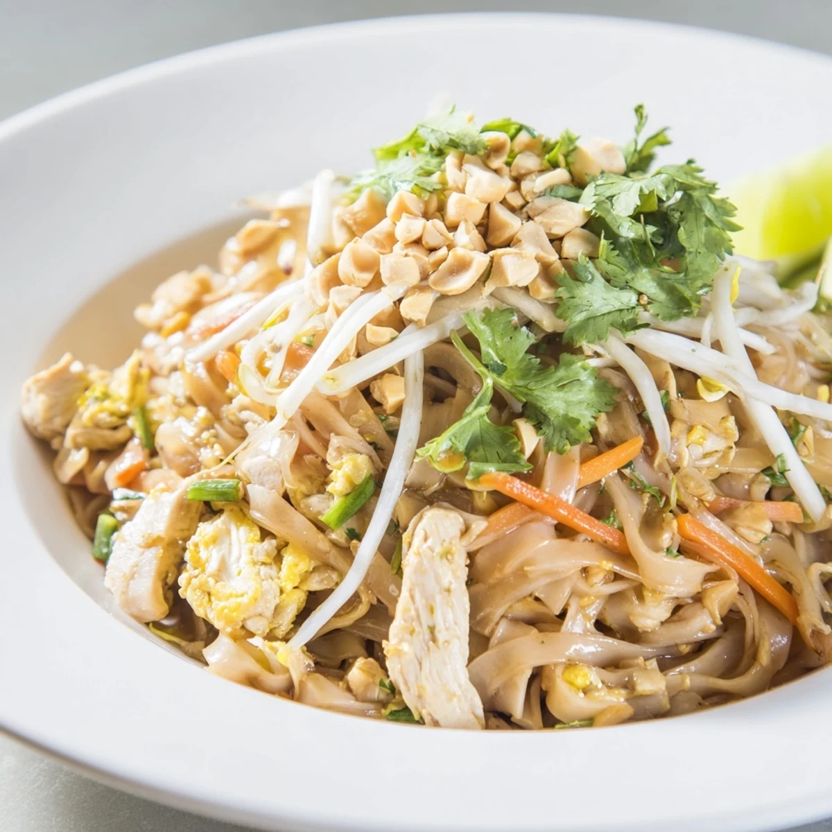 Golden chicken pad Thai tossed with rice noodles in tangy tamarind sauce, topped with crushed roasted peanuts and fresh lime.