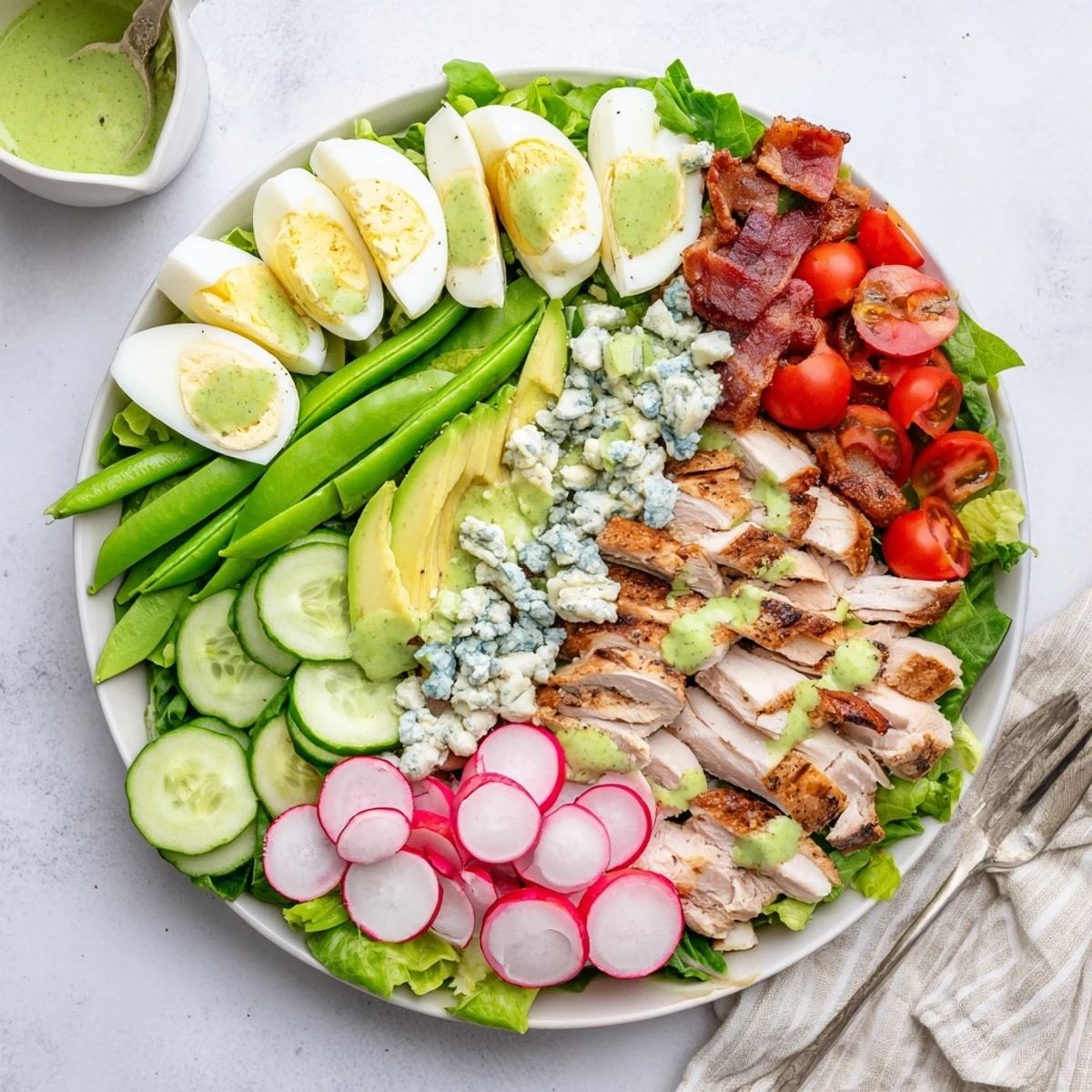 Fresh Spring Cobb Salad arranged with grilled chicken, bacon, avocado, and crisp vegetables on a white platter