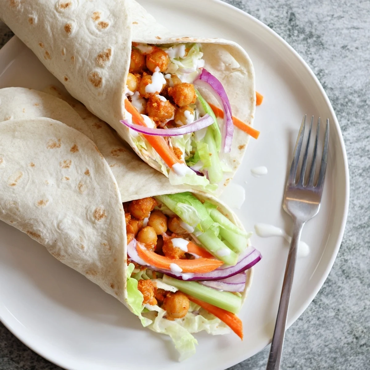 Homemade buffalo chickpea wraps topped with crunchy celery, red onion, and drizzled dressing