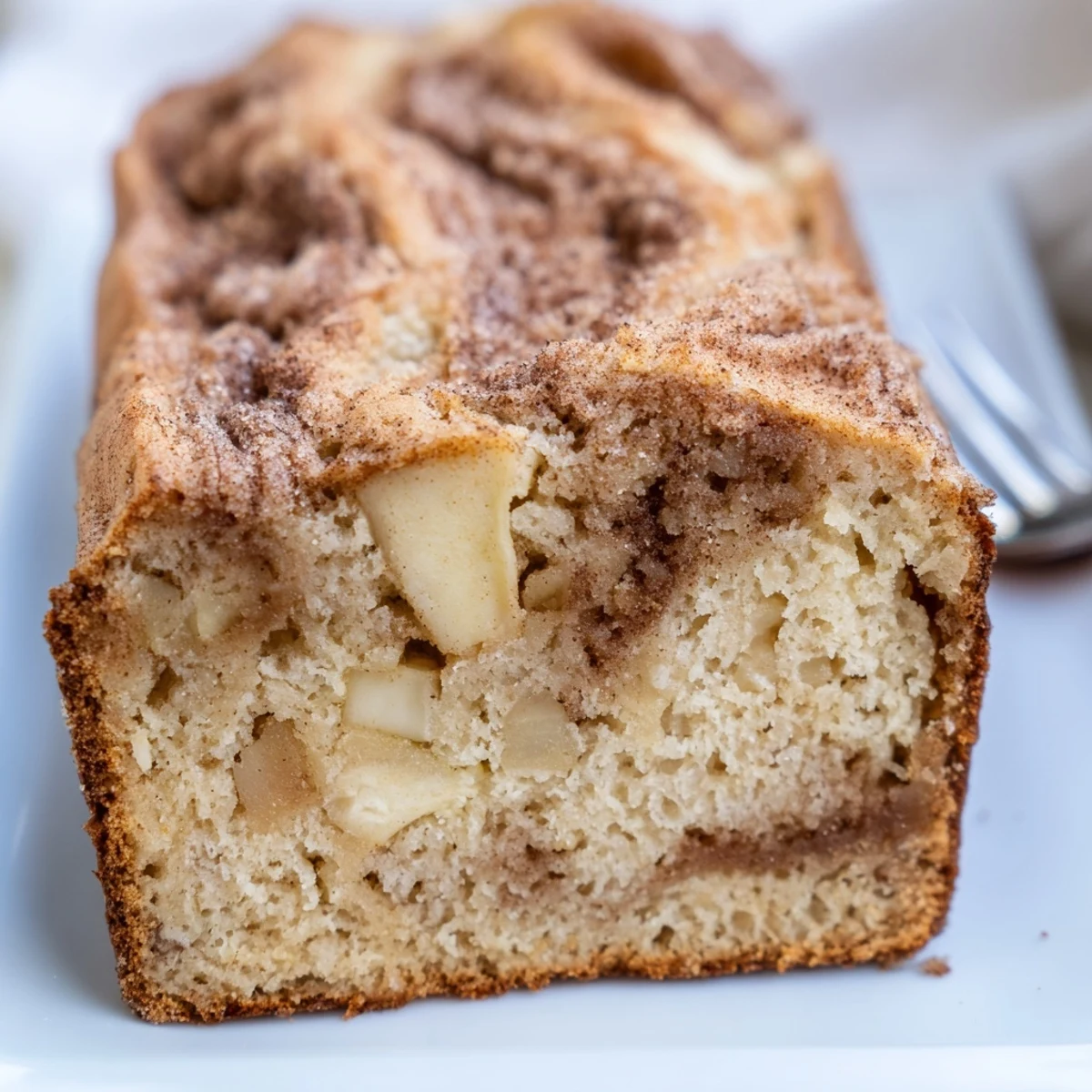 Golden cinnamon apple bread loaf with visible apple chunks and swirled cinnamon sugar topping on a wooden board