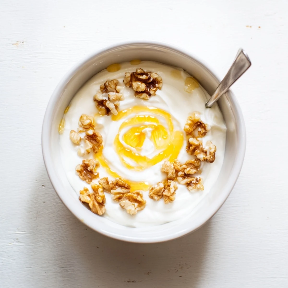 Thick creamy homemade Greek yogurt in a white bowl topped with fresh honey and walnuts