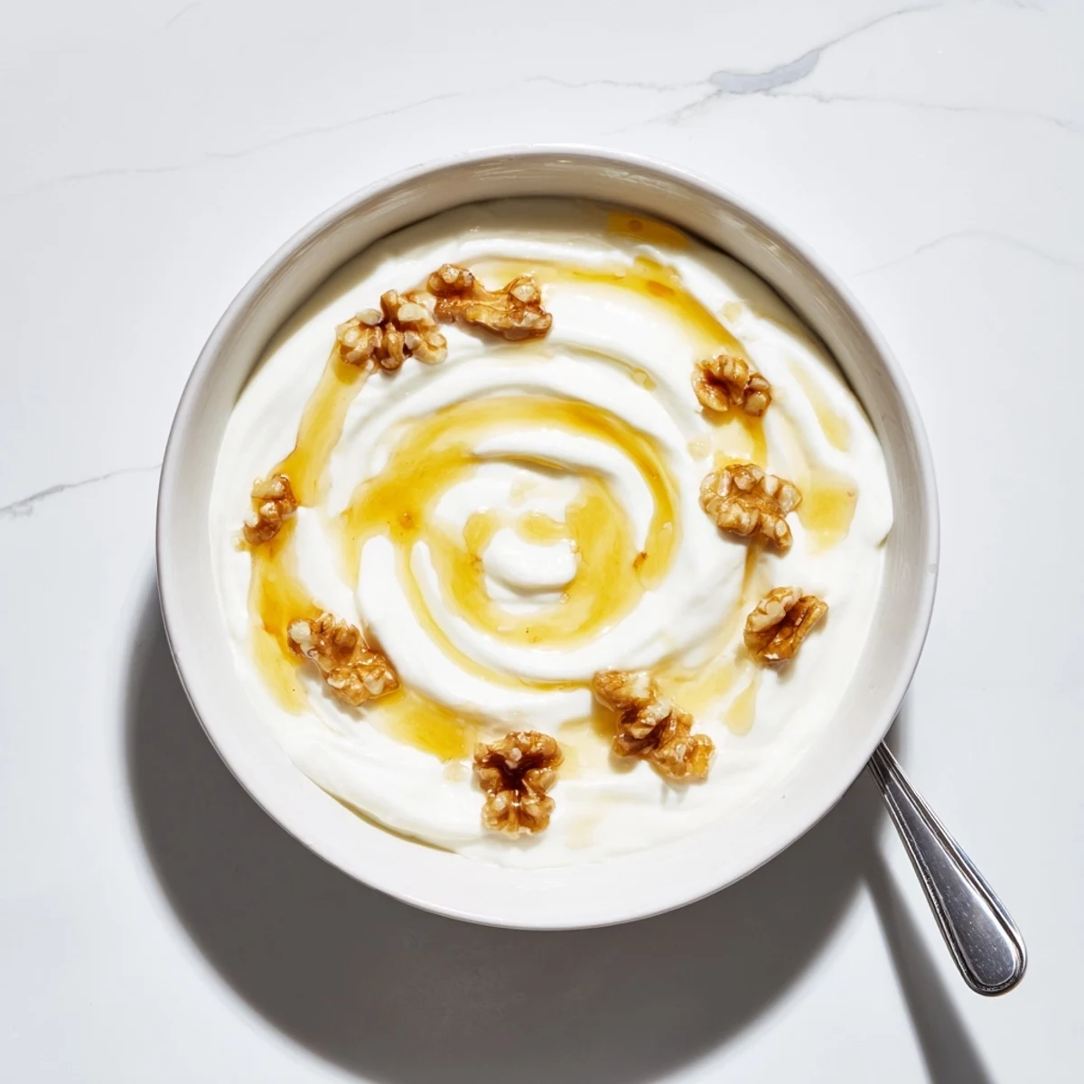 Smooth tangy Greek yogurt spooned into a glass jar with a drizzle of golden honey