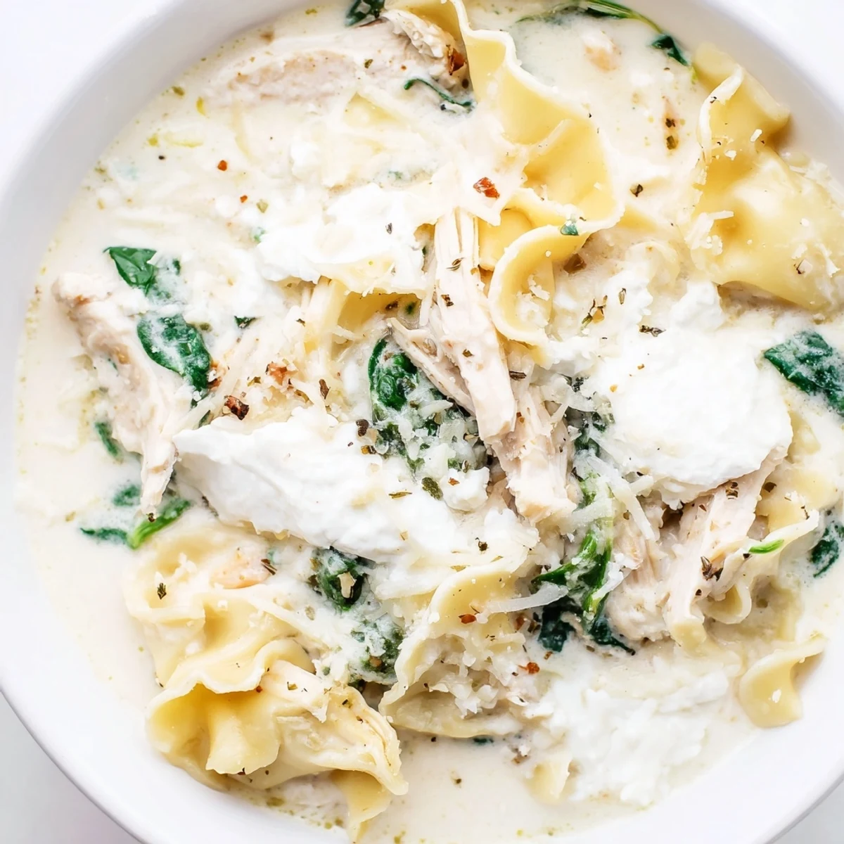 Steaming bowl of white lasagna soup topped with parmesan and cracked black pepper