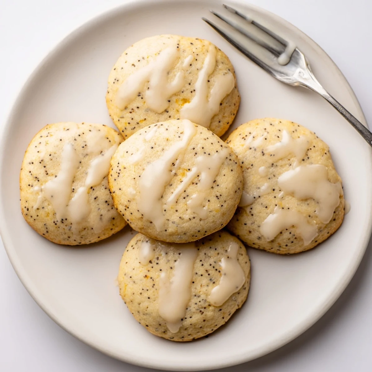 Golden lemon poppy seed cookies with crackly tops drizzled with sweet citrus glaze on a white plate