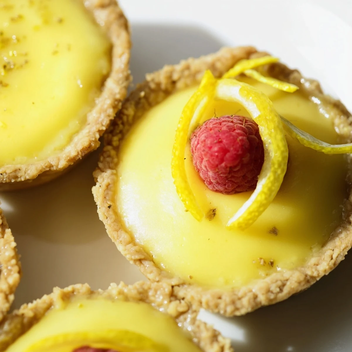 Golden mini vegan lemon tarts topped with fresh berries on a rustic white serving plate