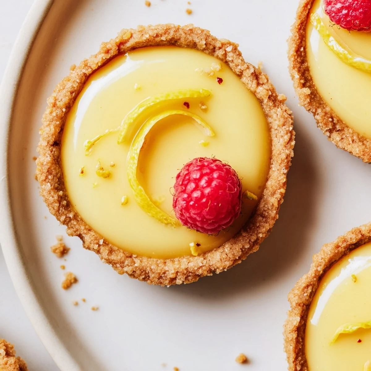 Creamy vegan lemon tarts in crisp almond crusts garnished with delicate lemon zest curls