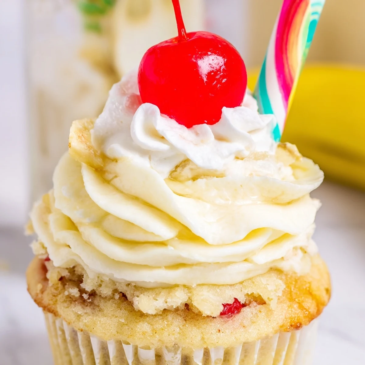 Golden banana milkshake cupcakes topped with creamy vanilla frosting and bright red cherries