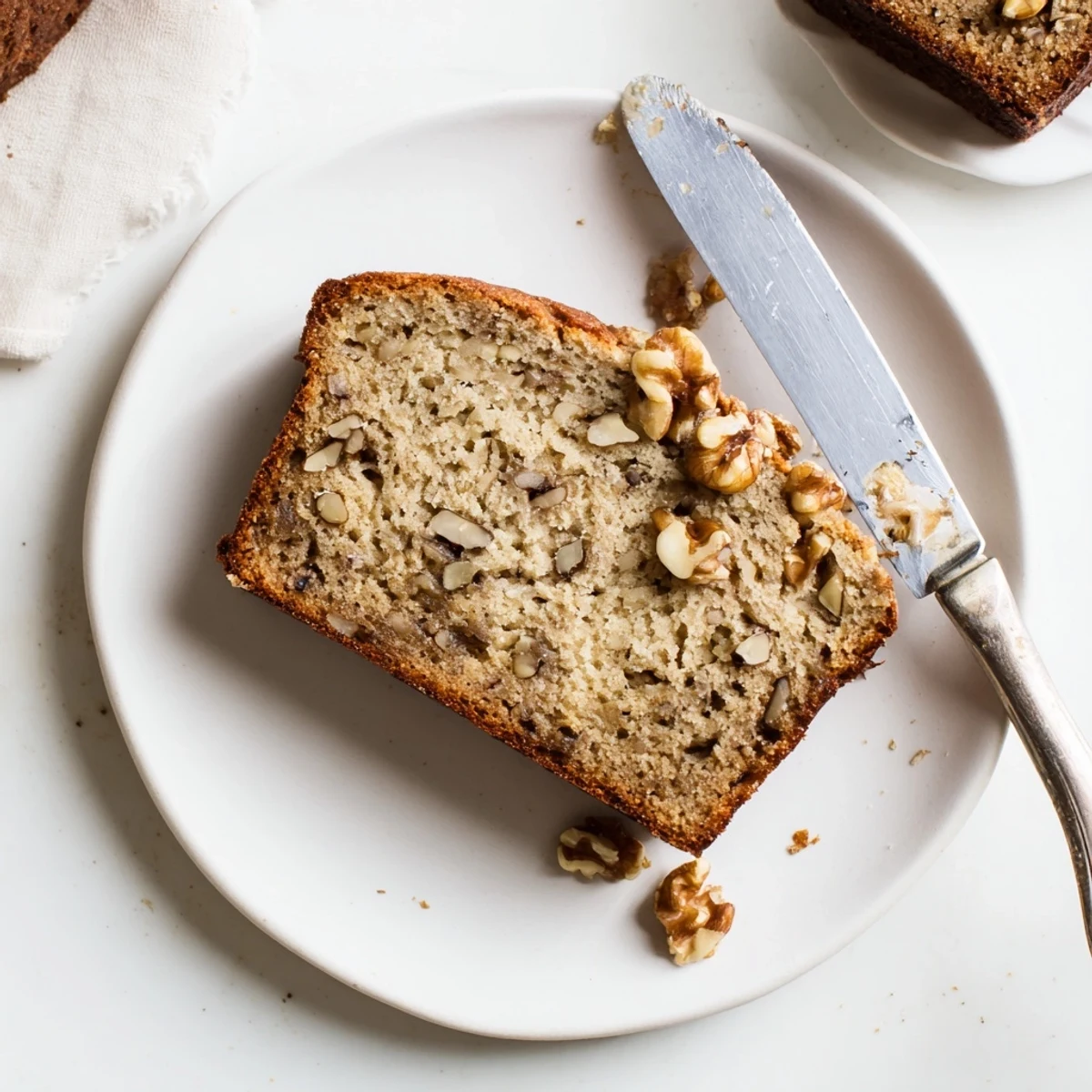 Golden banana nut bread loaf sliced on a rustic cutting board with scattered walnuts