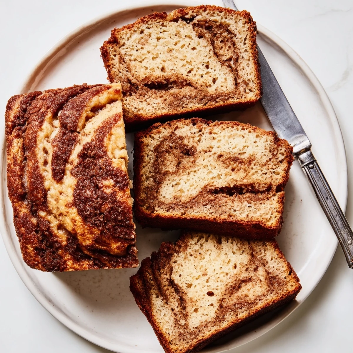 Golden snickerdoodle banana bread loaf sliced on a rustic cutting board with cinnamon-sugar swirl visible inside