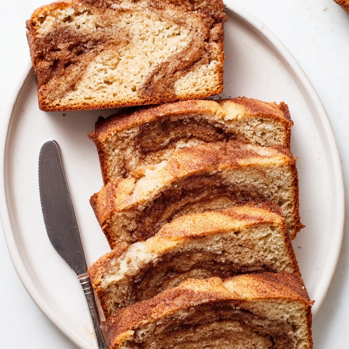 Warm slice of snickerdoodle banana bread topped with melting butter next to a steaming coffee mug