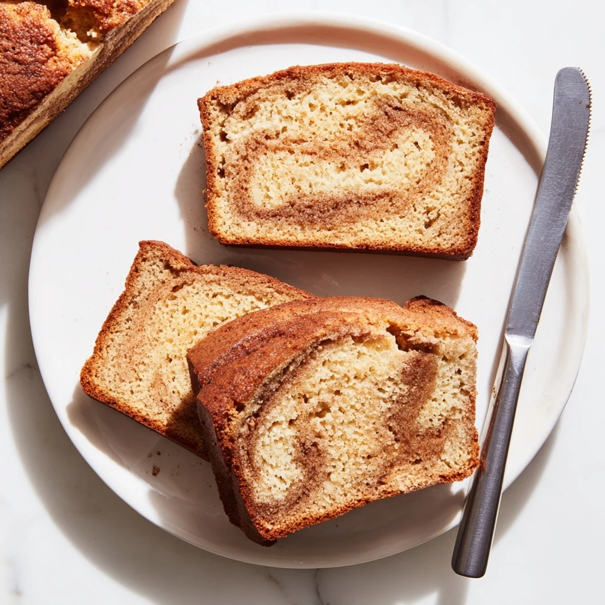 Moist snickerdoodle banana bread with a crackly cinnamon-sugar crust served on a white dessert plate