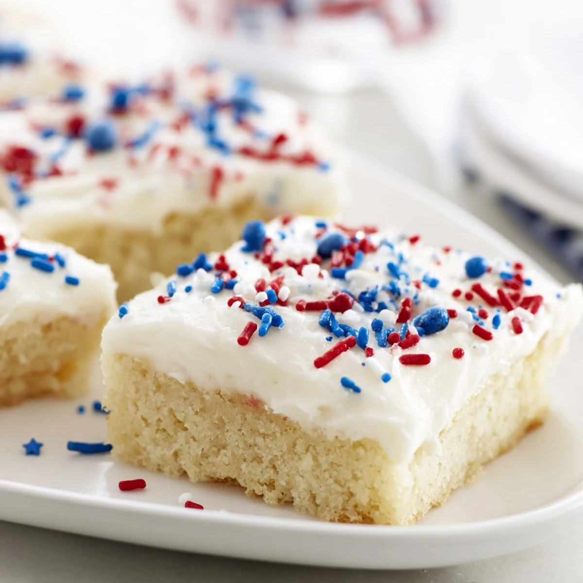 Golden baked 4th of July sugar cookie bars spread with vanilla buttercream frosting and festive sprinkles on a white serving platter