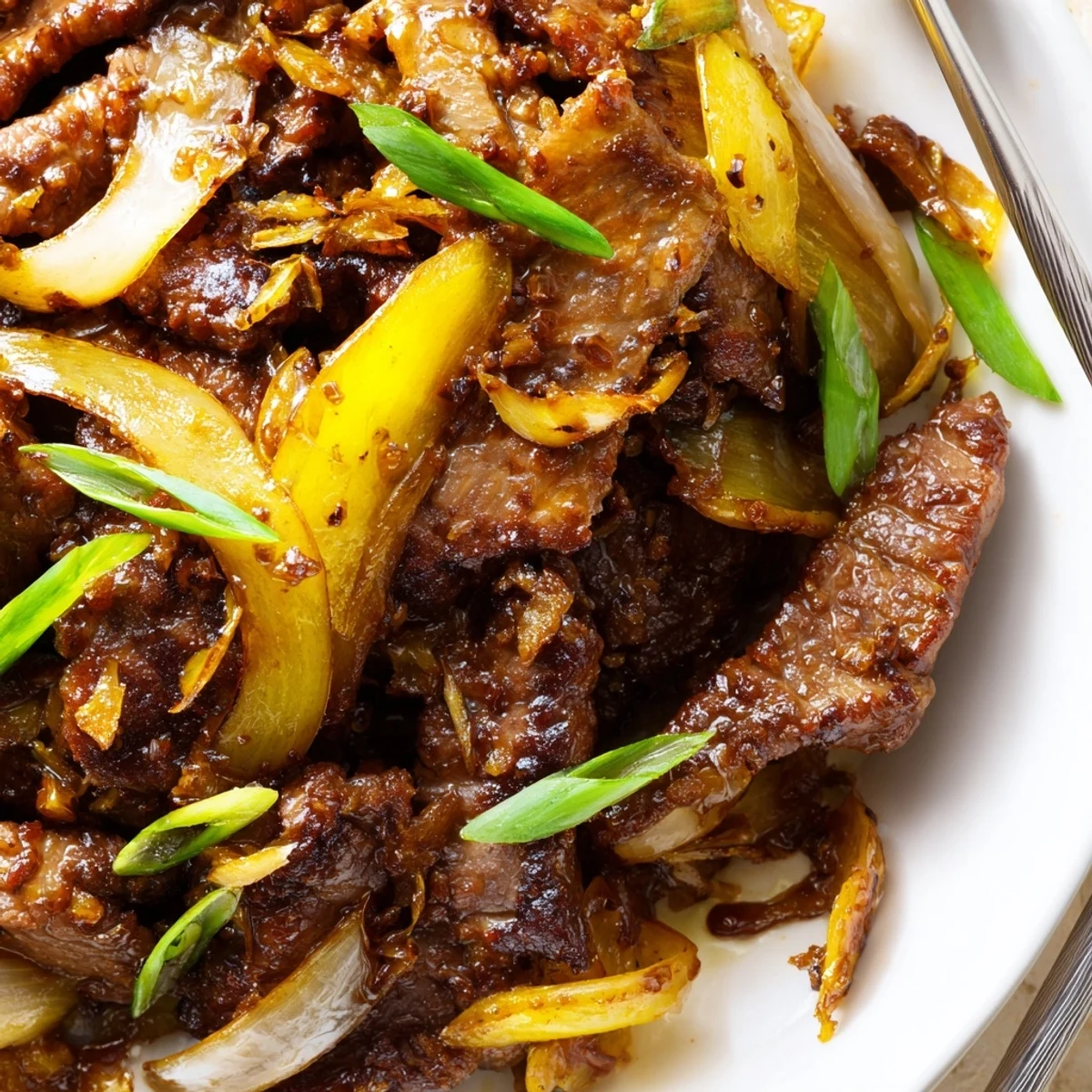 Plate of crispy beef and onion stir fry garnished with fresh green onions
