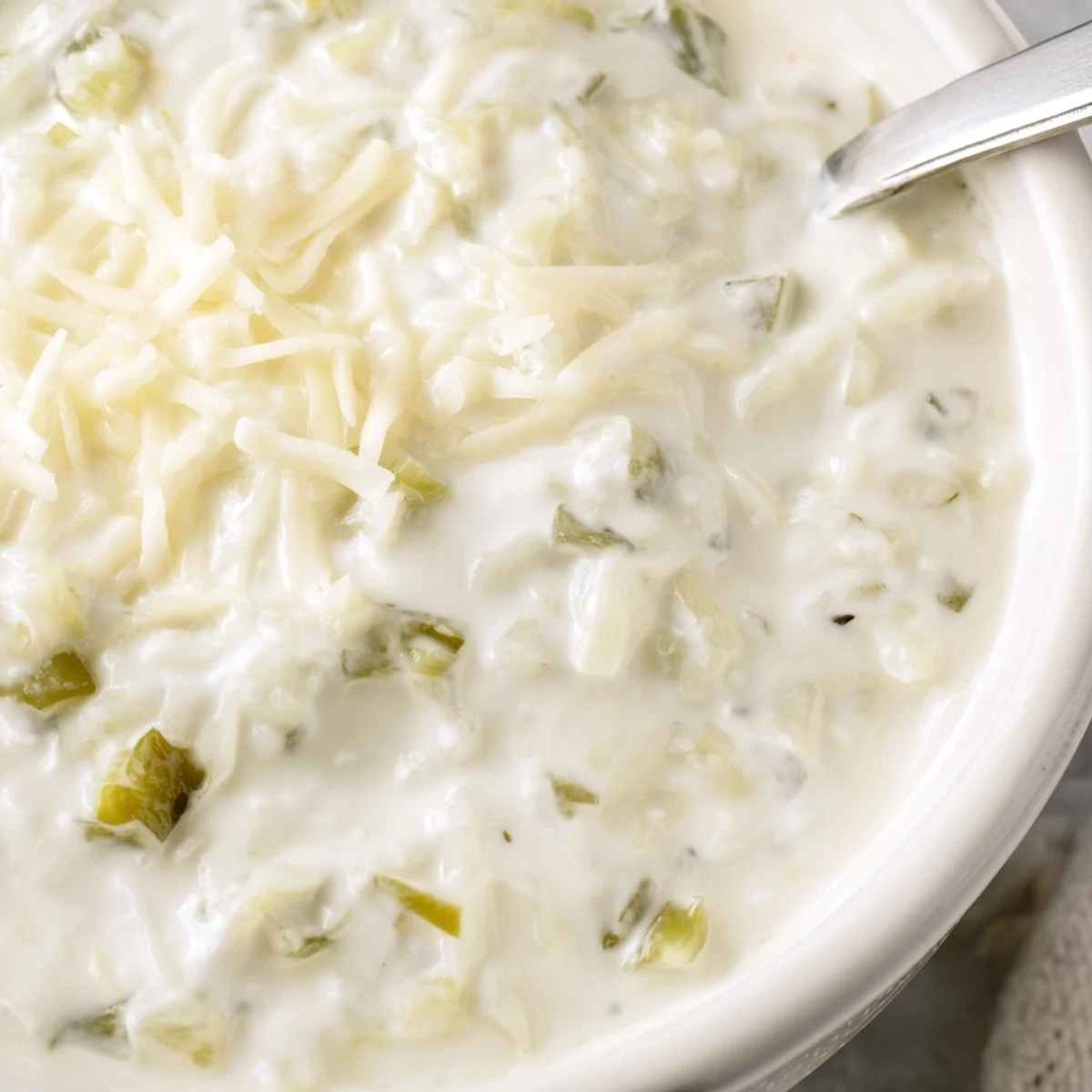Rich white queso dip bubbling in a bowl with scattered jalapeños and tortilla chips.